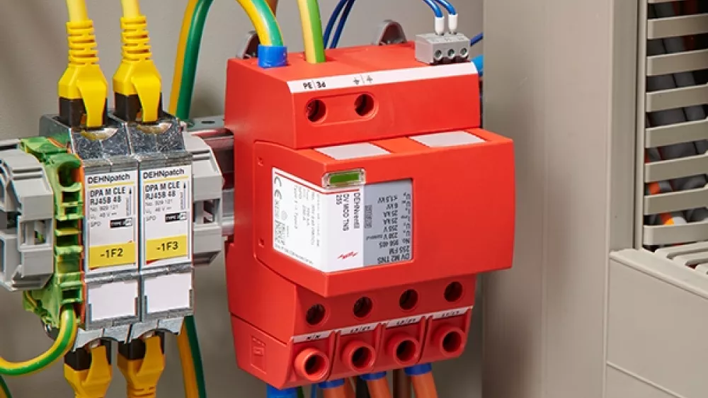 Scaricatore di sovratensioni rosso montato e cablato accanto a un quadro elettrico aperto.